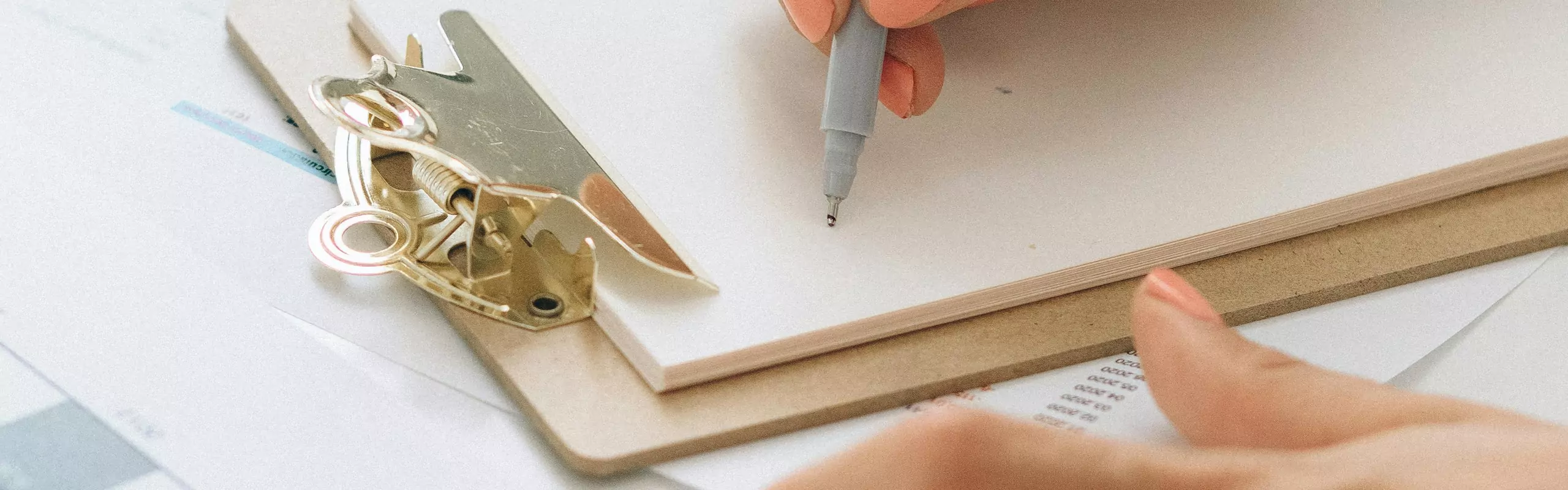 Person writing on white paper on a clipboard