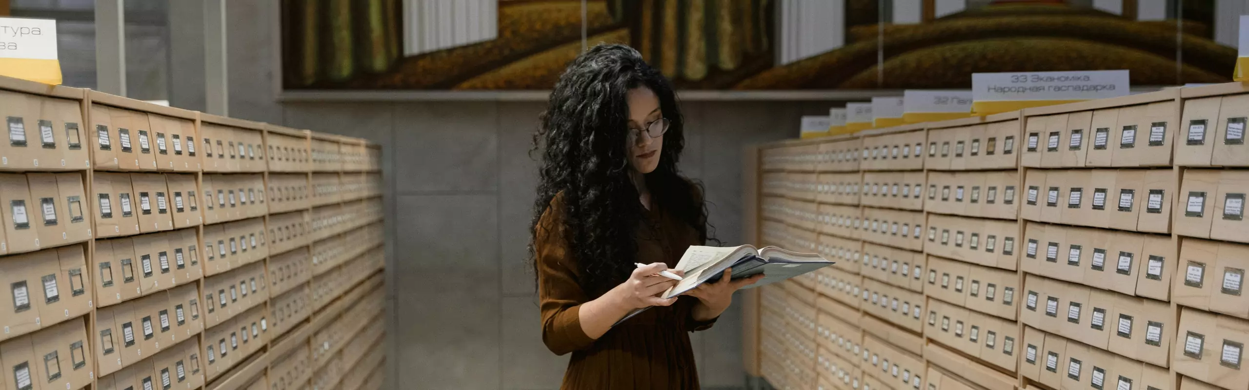 Woman reading a book between archive drawers
